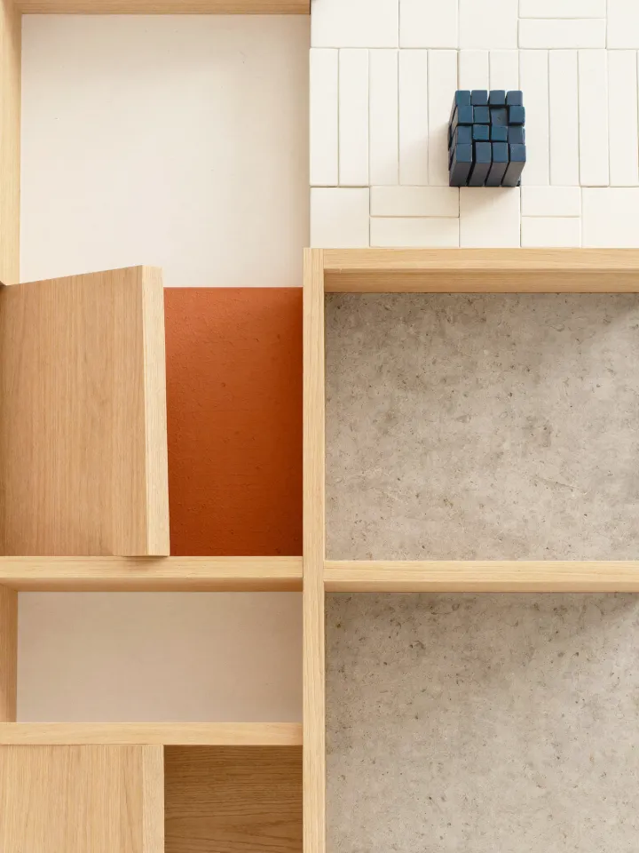 Maqueta cenital de materiales en compartimentos —roble, microcemento y un acento en terracota—, una pieza por formación.